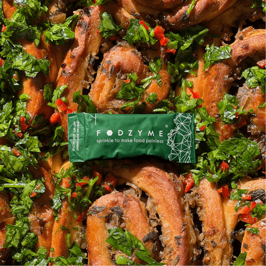 FODZYME single-serve packet reading 'sprinkle to make food painless' resting on a dish of garlic bread with herbs and chili.
