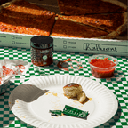 FODZYME enzyme powder jar and single-serve packet alongside a pizza box and tomato dipping sauce on a green checkered tablecloth.